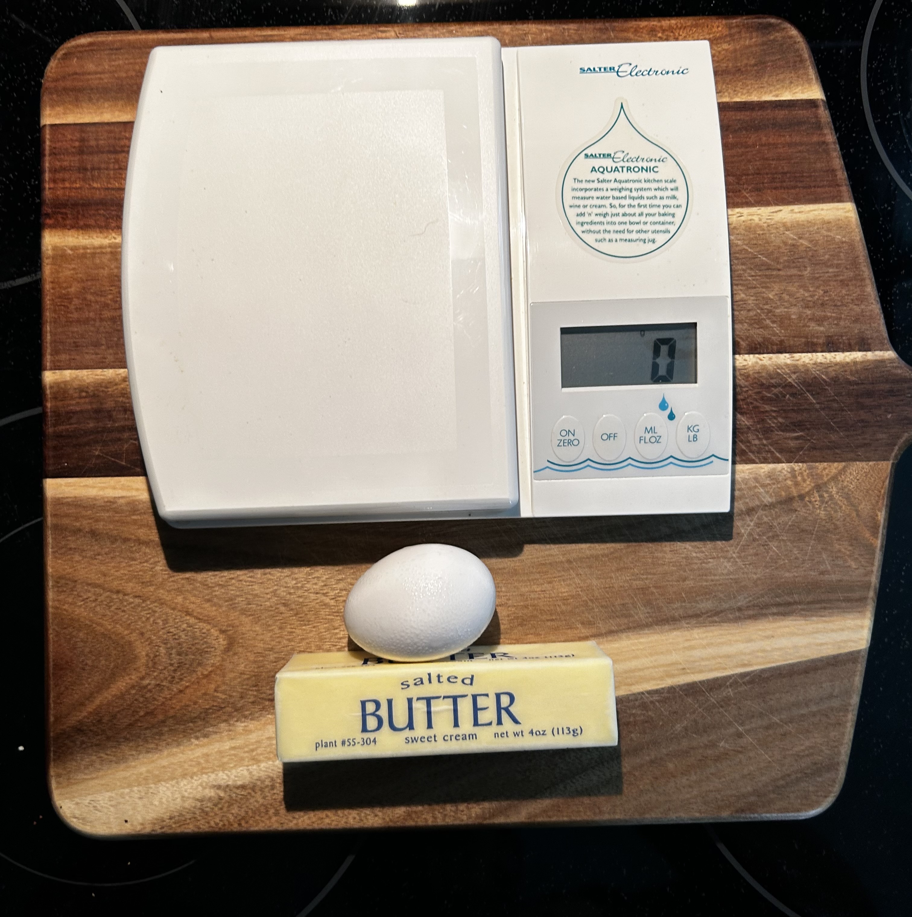 Egg resting on a stick of butter beside a kitchen scale for testing the old recipe measurement “butter the size of an egg.
